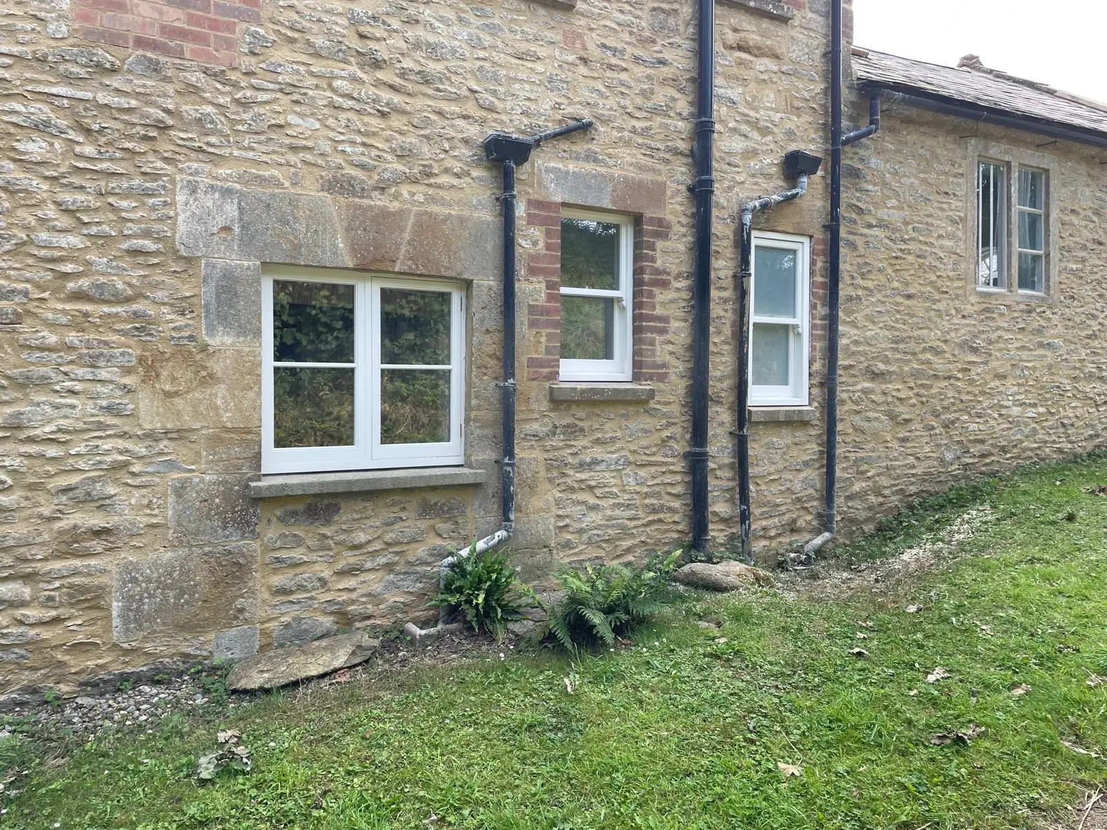 White timber casement windows fitted into a honey-coloured Dorset stone cottage
