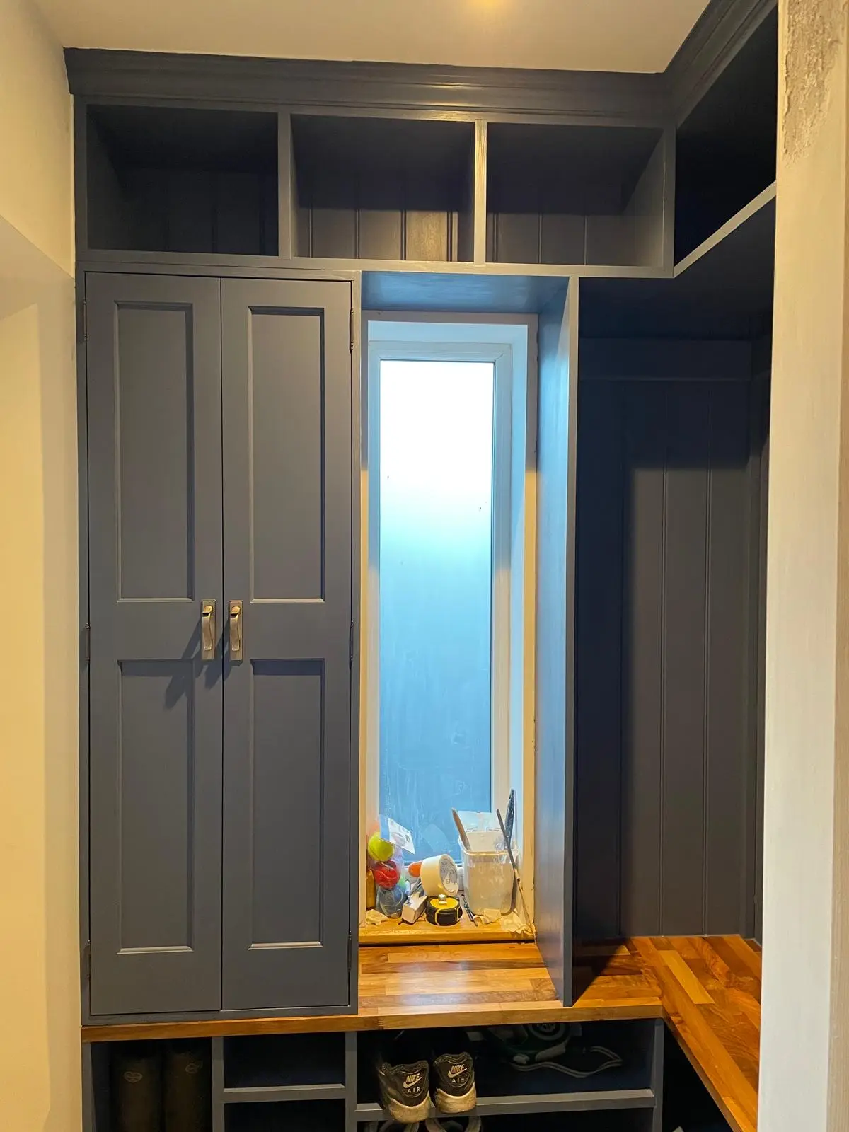 Fitted navy boot room with shaker cupboards, oak bench worktop, open cubbies and shoe storage