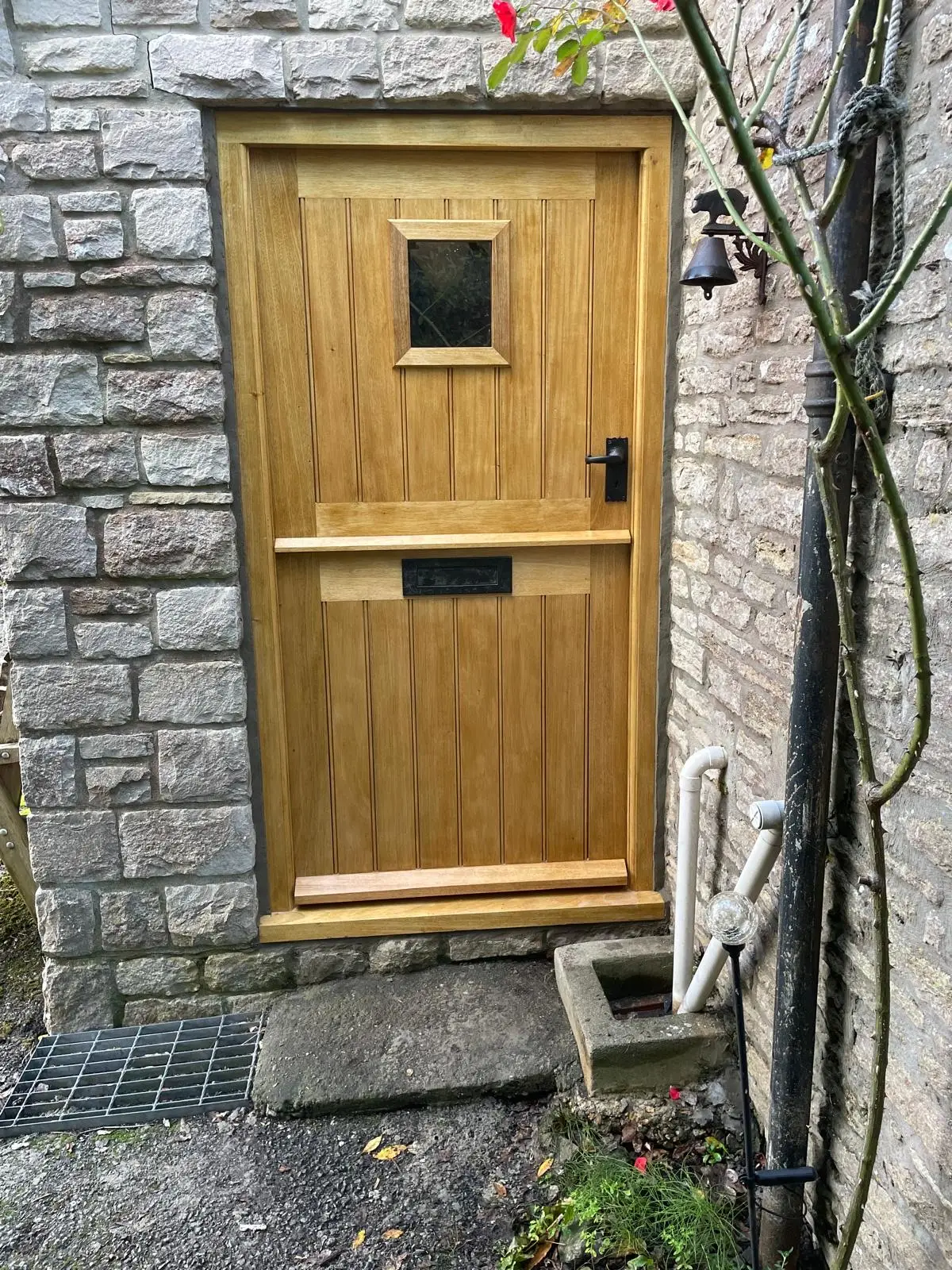 Installed bespoke oak stable door with glazed light and black ironmongery in a stone cottage wall