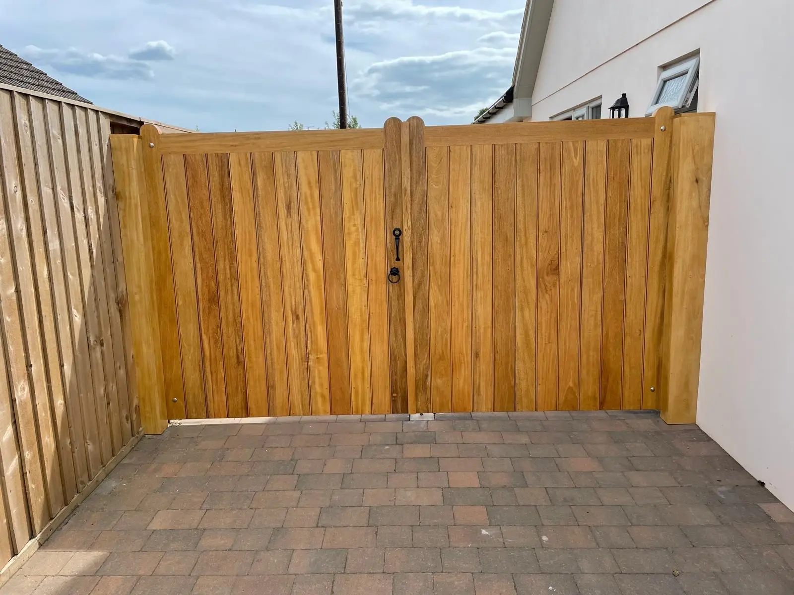 Curved-top hardwood driveway gates with a ring latch on a block-paved drive