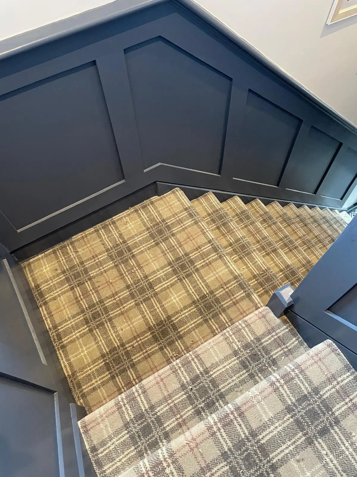 Tartan wool stair runner on a winder staircase with deep navy panelled walls, seen from above