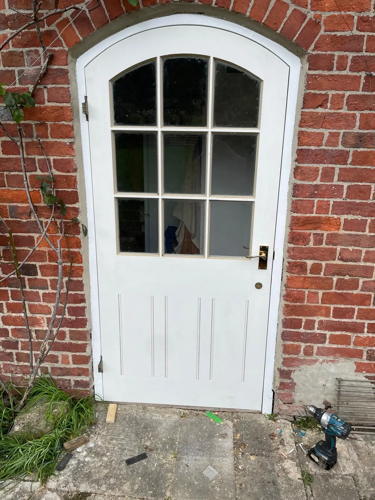 Arched white-painted timber back door with nine glazed panes set in a red-brick wall
