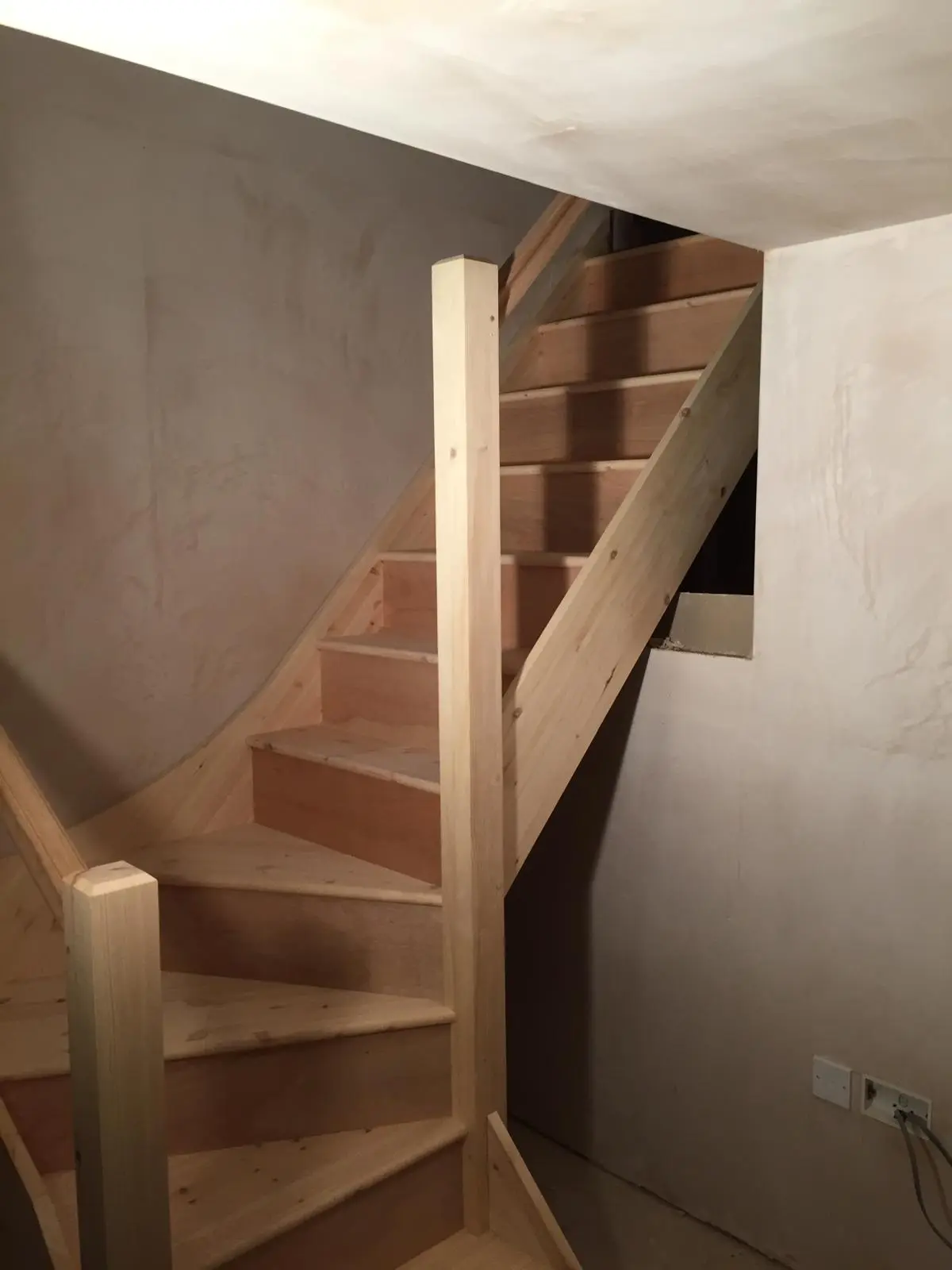 Winder staircase in pine with newel posts and handrail, fitted against freshly plastered walls