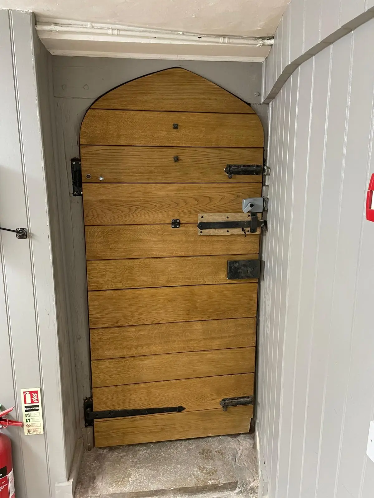 Arched oak boarded door with black strap hinges and a latch in a panelled doorway