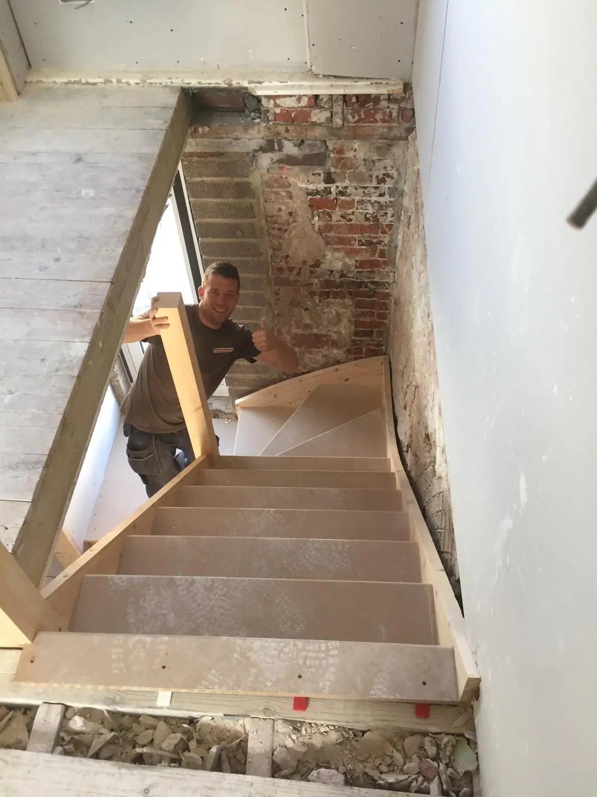 A joiner fitting a winder staircase into a period house, with the original brickwork exposed alongside the new treads